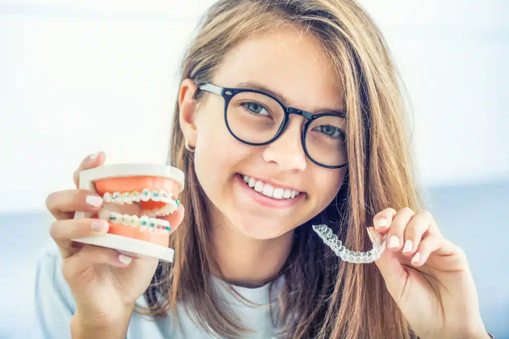 child holding two types of braces (metal and invisible) in her hands.