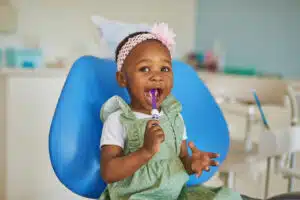 young girl smiling and brushing her teeth in a dentist chair.